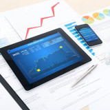 Modern business workplace with stock market data on a digital tablet, mobile banking on a smartphone and many charts and graphs on a desktop.